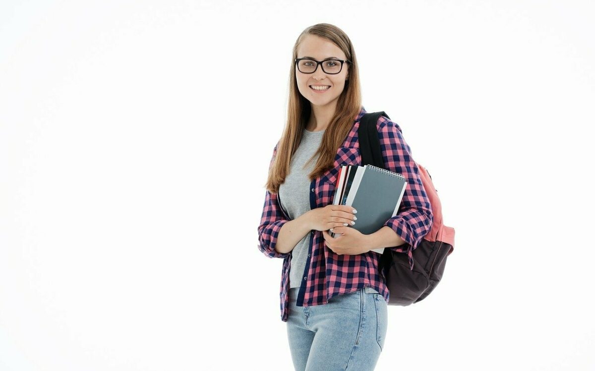 Eine junge Frau mit Rucksack auf dem Rücken und Büchern im Arm lächelt in die Kamera Eine junge Frau mit Rucksack auf dem Rücken und Büchern im Arm lächelt in die Kamera
